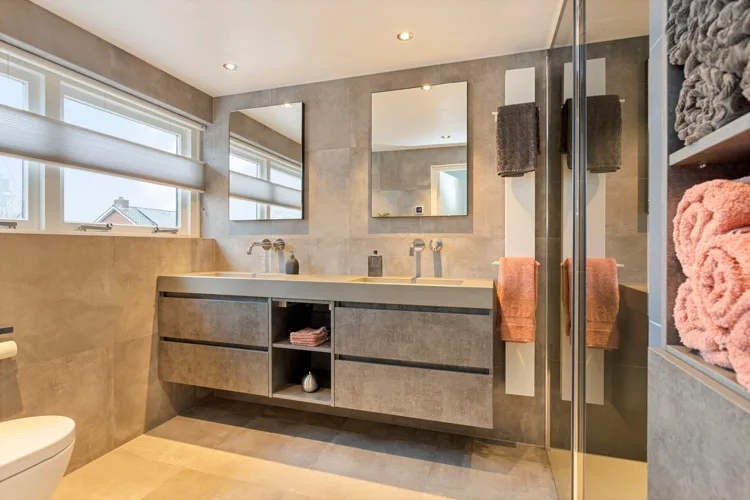Warme badkamer met dubbele waskom, hout en beige tegels.