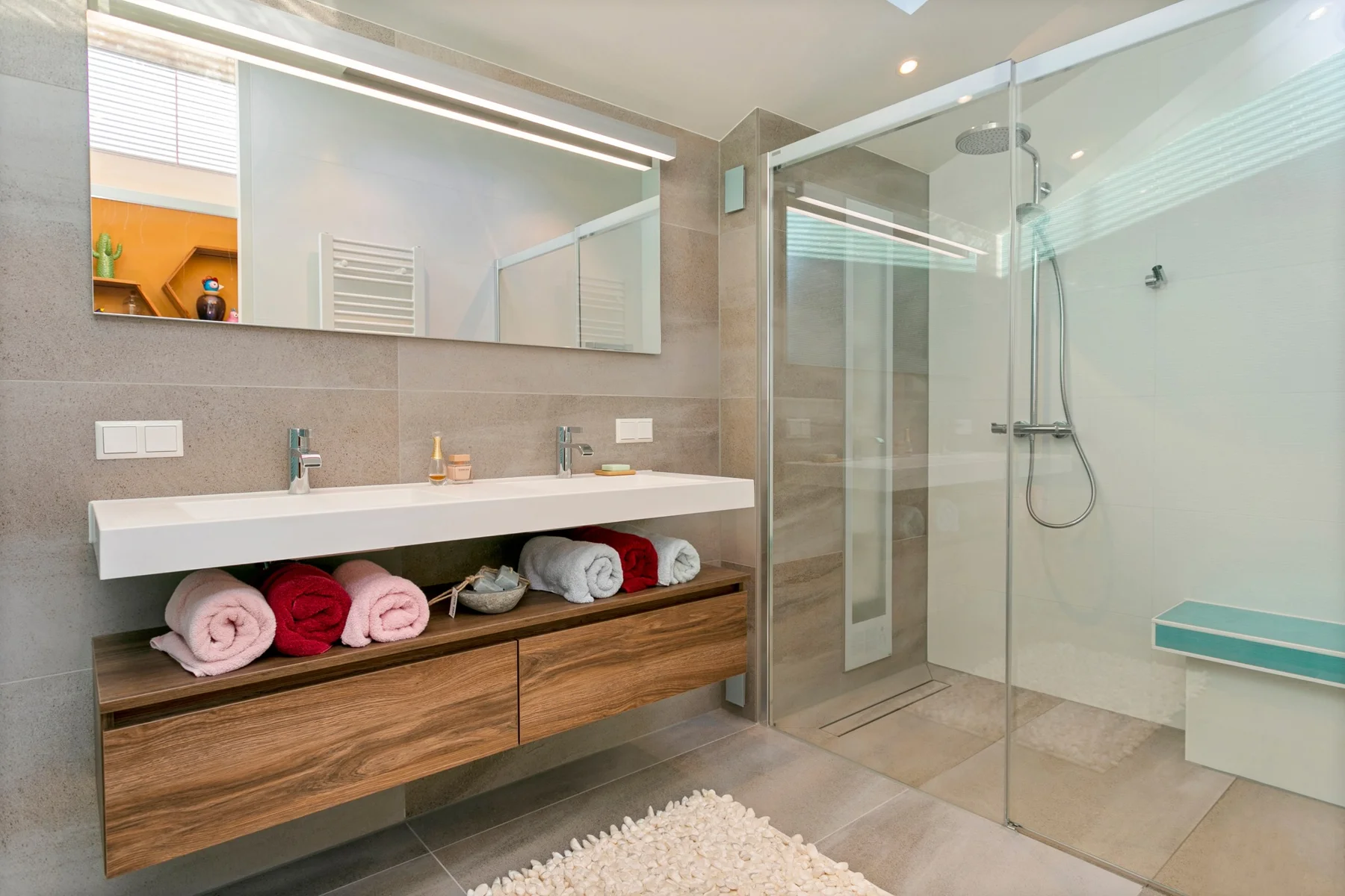 Badkamer met houten meubel, open handdoekenvak en glazen douche.
