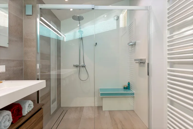 Smalle douche met glazen wand en lichte tegels.