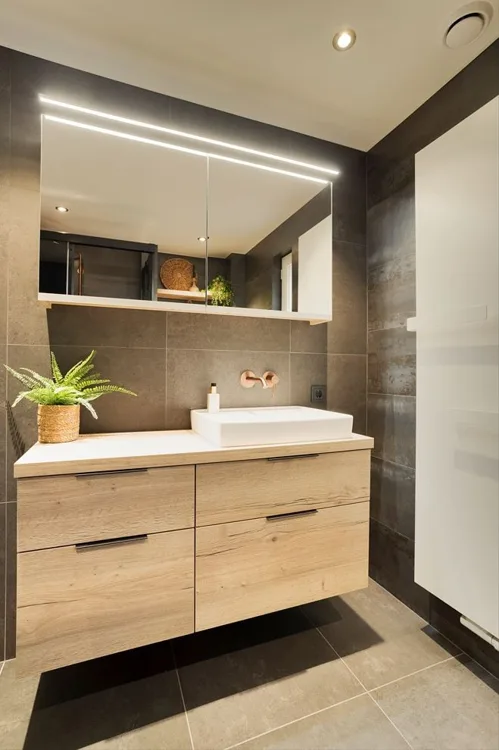Smalle badkamer met houten meubel en subtiele verlichting.