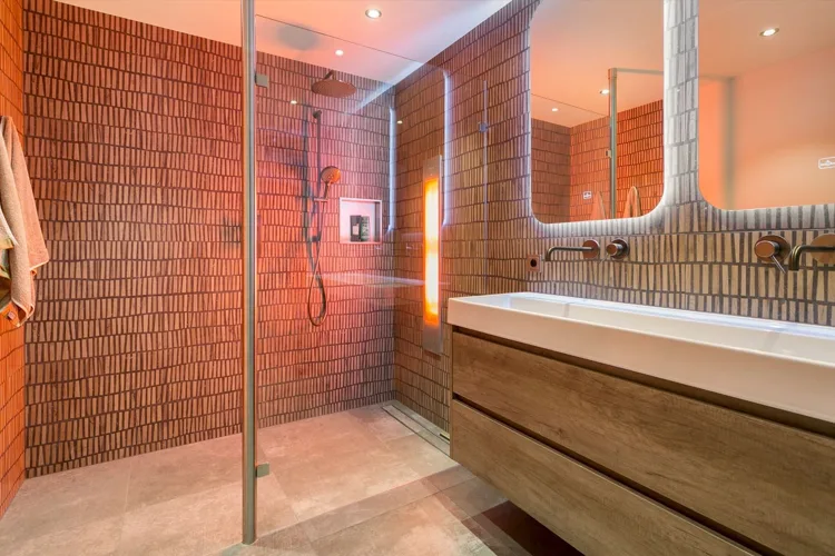 Badkamer met warme verticale tegels en een houten meubel.