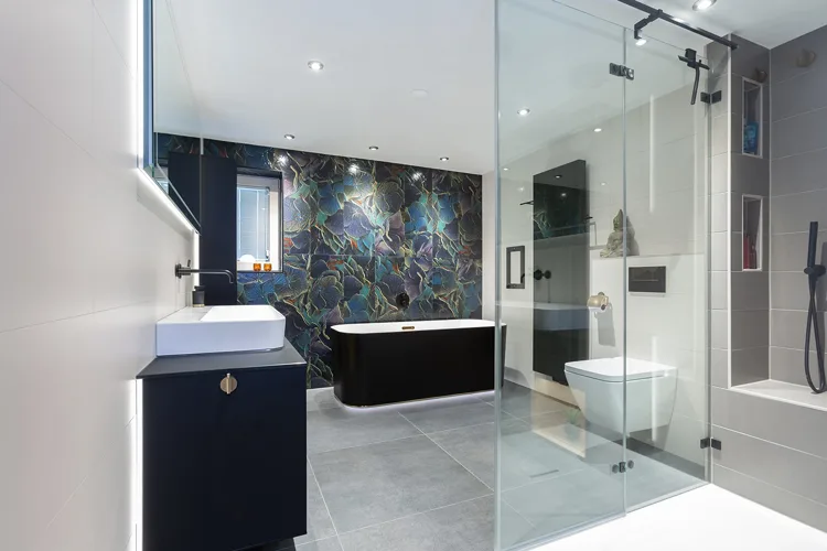 Ruime badkamer met donker bad en expressieve tegelwand.